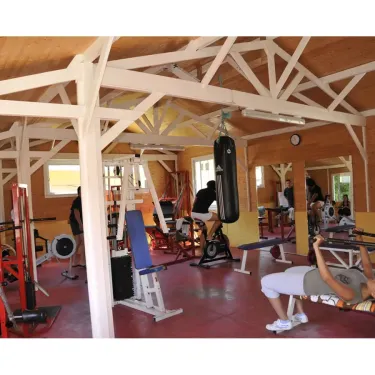 Salle de sport en bois avec équipements de musculation et personnes en train d'exercer.