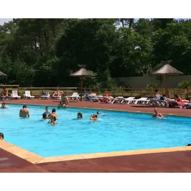Piscine entourée de transats sous parasols en paille au Camping La Pointe.