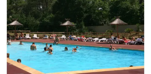 Piscine entourée de transats sous parasols en paille au Camping La Pointe.