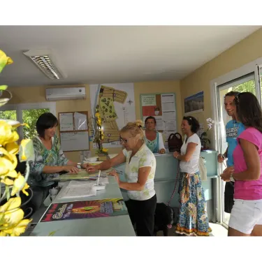 Reception du camping La Pointe avec trois femmes et un chien noir près du comptoir.