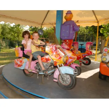 Deux enfants sur une moto de jeu colorée dans le parc d'attractions du Camping La Yole.