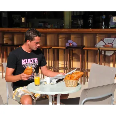Un homme dégustant un jus d'orange et un pain au Café Camping La Yole.
