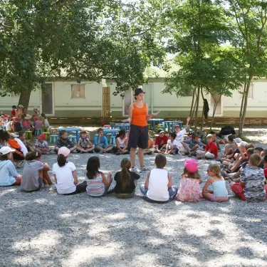 Enseignante parlant devant un groupe d'enfants assis autour d'elle dans le camping Le Castellas.