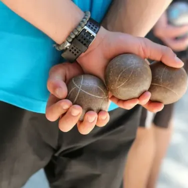 Main tenant des boules de pétanque en pierre au Camping du Lac de Miel.