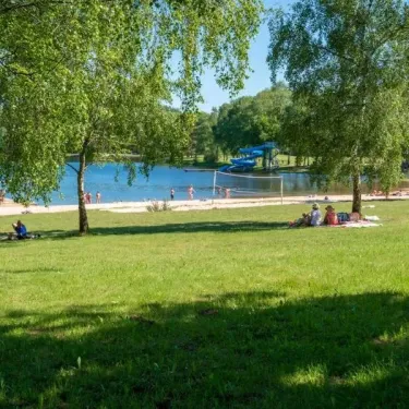 Lac avec plage, arbres et personnes se détendant au Camping du Lac de Miel