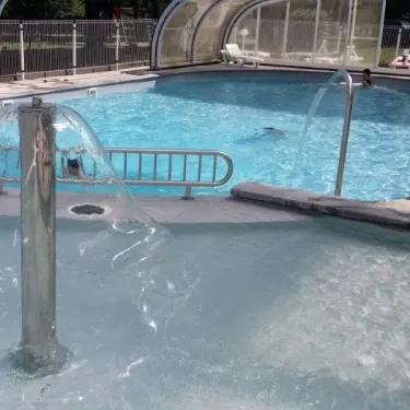 Piscine avec fontaine et enfants nageant au Camping du Lac de Miel