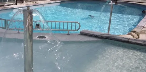 Piscine avec fontaine et enfants nageant au Camping du Lac de Miel