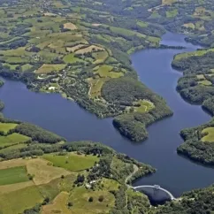 Vue aérienne du lac entouré de collines et de champs à Camping La Romiguière