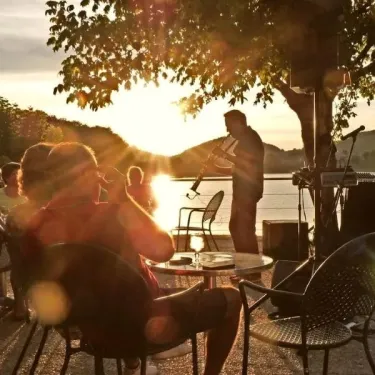 Musicien joue devant un public assis en plein air, au coucher du soleil sur le lac à Camping La Romiguière.