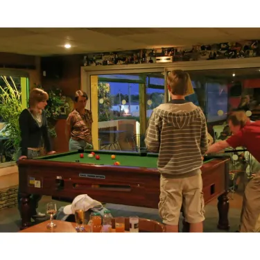 Camping Le Pré Catalan : groupe jouant au billard dans une salle lumineuse avec fenêtres ouvertes.