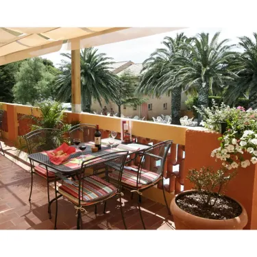 Camping Le Pré Catalan : balcon avec table dressée, chaises, palmiers et fleurs en pot sous un auvent.