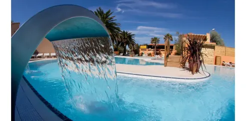 Piscine avec chute d'eau et palmiers au Camping Le Pré Catalan