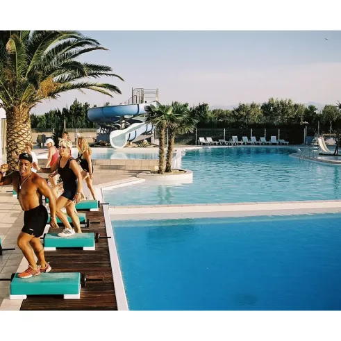 Camping Mar i Sol : piscine avec toboggan, palmiers et personnes faisant de l’exercice sur des planches flottantes.