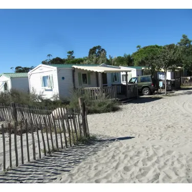 Camping Marina d'Aléria avec mobil-homes blancs sur plage de sable sous un ciel bleu.
