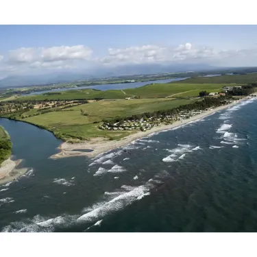 Vue aérienne du Camping Marina d'Aléria le long d'une côte avec océan, rivière et champs verts.