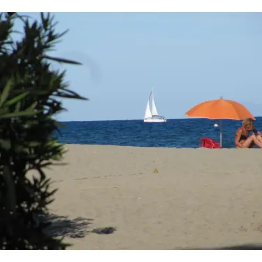 Plage avec parasol orange et voilier à l'horizon au Camping Marina d'Aléria