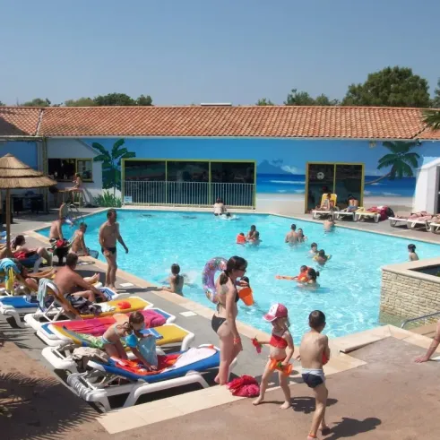 Camping Oléron Loisirs : piscine avec enfants et adultes, chaises longues et palmiers.