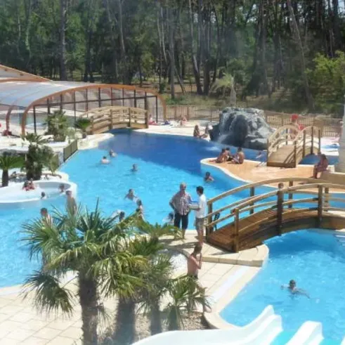 Piscine extérieure avec pont en bois et palmiers au Camping Soulac Plage