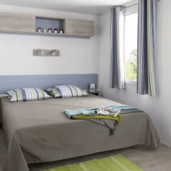 Mobil Home Mercure 2Ch – 4P - Camping du Val : Chambre avec lit double et rideau à rayures