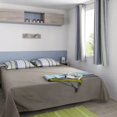 Mobil Home Mercure 2Ch – 4P - Camping du Val : Chambre avec lit double et rideau à rayures