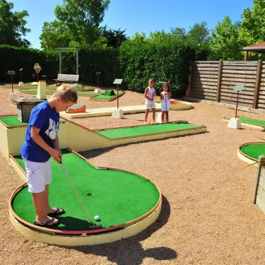 Enfant jouant au mini-golf dans une cour de Camping La Bollée d'Air