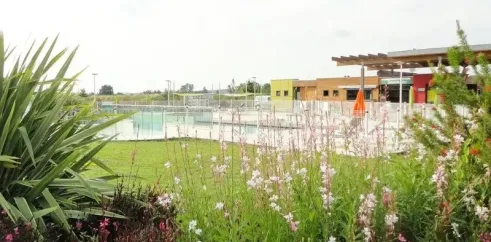 Piscine visible à travers un jardin fleuri au Camping Paradis Vallée du Lot