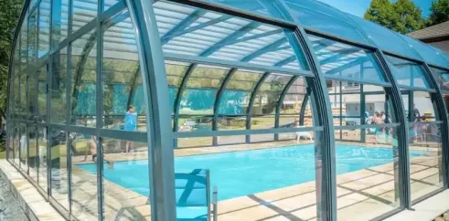 Piscine couverte au Camping Sous le Moulin, avec eau bleue et personnes en bord de piscine.