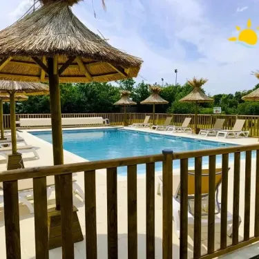 Piscine avec parasols en paille et chaises longues au Camping Le Plan d'eau