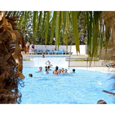 Camping Les Fontaines - Vue à travers les feuilles de palmier sur une piscine animée