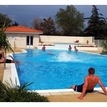 Camping Les Fontaines - Piscine avec enfants et adultes, palmier, bâtiment de gestion.