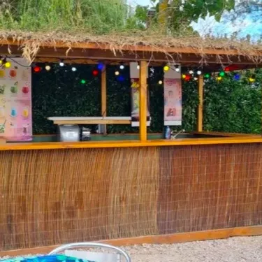 Bar tropical en bambou avec toit de paille et guirlandes lumineuses au Camping Le Bourdieu.