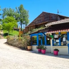 Camping Le Bourdieu - boutique en bois avec toit rouge et pots roses