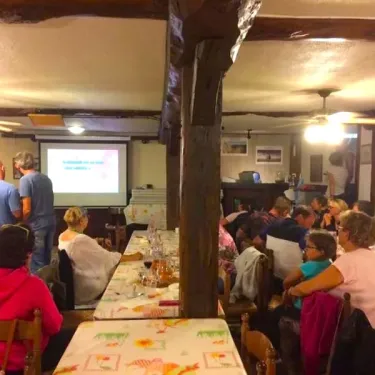 Camping Le Bourdieu : groupe dans une salle à la charpente en bois, projection sur écran.
