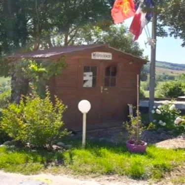 Boutique du camping Le Bourdieu avec drapeaux français et roumain, devant une cabane en bois.
