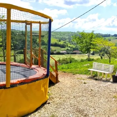 Camping Le Bourdieu - Trampoline et banc en plein air sur un terrain en gravier