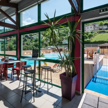 Camping La Cascade - salle à manger avec tables et chaises, vue sur la piscine