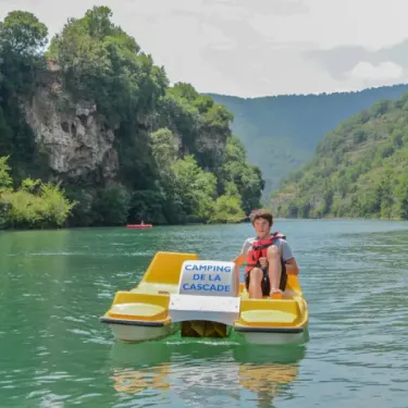 Enfant sur un canoë-pédalier avec l'inscription Camping La Cascade sur un lac
