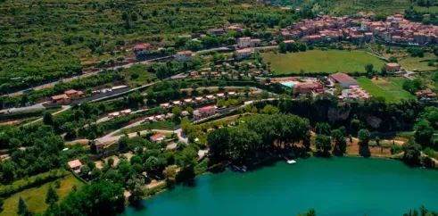 Vue aérienne d'un village niché près d'un lac turquoise, entouré de collines vertes et de routes serpentines.