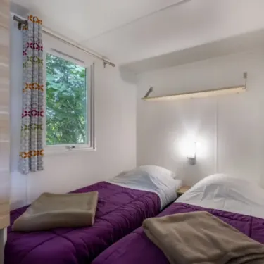 MH Classique 3CH - 6P - Camping Bel Air Village Le Plan d'eau : chambre avec deux lits et rideau coloré