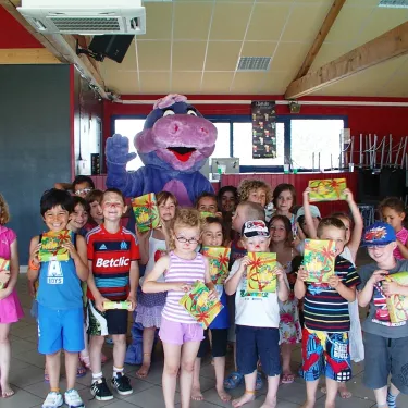 Enfants souriants devant un mascotte dinosaure au Camping Le Curtys.