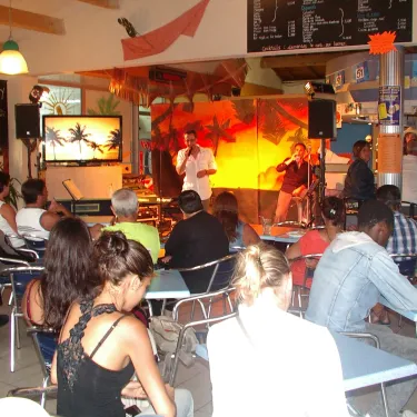Performance musicale sur scène dans un bar-restaurant du Camping Le Curtys, public attentif.