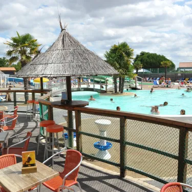 Terrasse avec parasol de paille et piscine au Camping Le Curtys