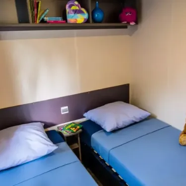 Mobil Home Confort Clim 2 Chambre TV - 4 Pers. - Camping La Croix du sud : deux lits simples, étagère avec jouets et livres