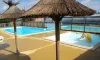 Piscine avec parasols en paille et toboggan jaune au Camping Les Hauts de Port Blanc