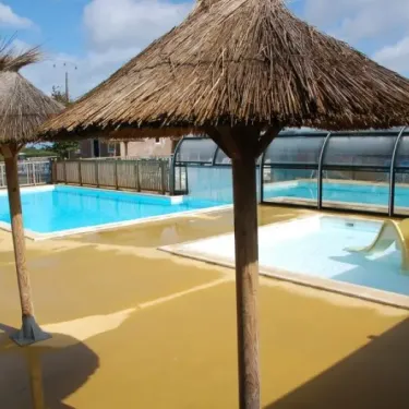 Piscine avec parasols en paille et toboggan jaune au Camping Les Hauts de Port Blanc