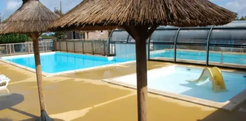Piscine avec parasols en paille et toboggan jaune au Camping Les Hauts de Port Blanc