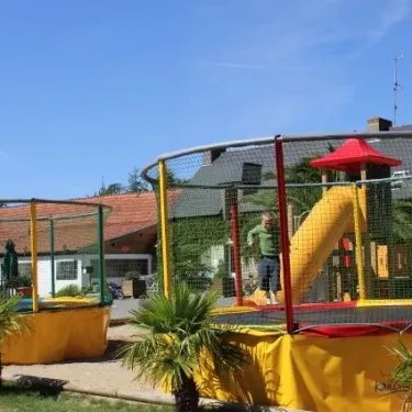 Enfant saute sur un trampoline encadré dans un parc infantile à Camping Les Sables de Cordouan.