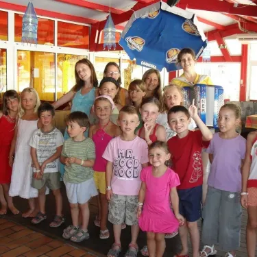 Enfants et adultes souriants devant un kiosque rouge à Camping Les Sables de Cordouan.