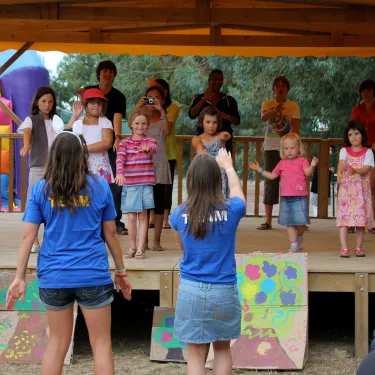 Enfants dansent sur une scène extérieure à Camping Les Sables de Cordouan, entourés d'adultes applaudissant.
