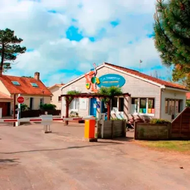 Entrée du camping Le Bosquet avec barrière, panneau d'information et bâtiments